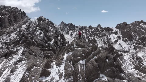 Slow motion drone shot of alone hiker man climbing on snow capped mountain peak Stock Footage 310219093