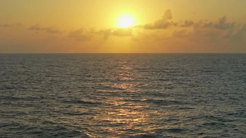 Slow-motion drone shot over the ocean at sunrise. The horizon glows with or.. Stock Footage 284872459