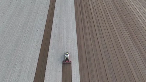 Slow-motion drone shot of tractor leveling striped fields near Maginot wetlands Stock Footage 308443559