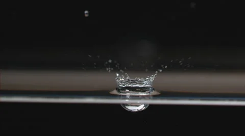 Slow motion, drop falls to water surface, splashing into droplets and ripples Stock Footage 63841103