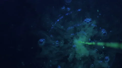 Slow motion. Drops of green fluorescent paint fall into black water. 库存影片 133713382