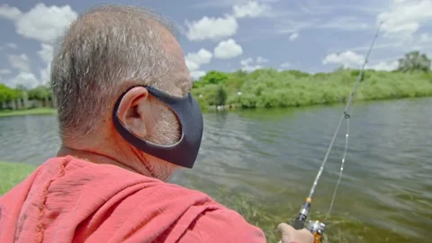 Slow motion of elderly man wearing face mask while fishing on a lake Stock Footage 131059829