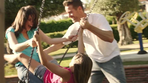 Slow motion of family in park father pushing mother and daughter on swing. Stock Footage