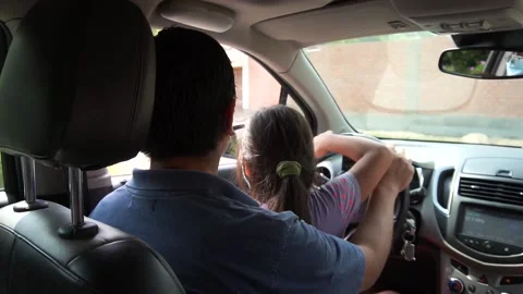 Slow motion of a father teaching his little daughter to move the wheel of a car Stockbeeldmateriaal 150926472