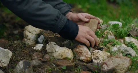 Slow motion fingers close around tan rock amid stones in Ötschergräben fire Видео 325955439