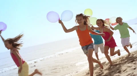 Slow motion of five children running by camera on beach holding balloons. Stock Footage 43672815