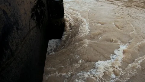 Slow motion flooded river filled with brown dirty water spilling under floodgate Stock Footage 120749347