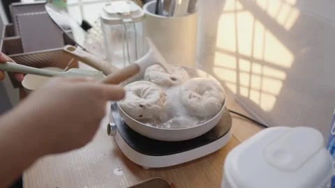 Slow motion footage of hands boiling homemade bagels in small pan on an electric Stock Footage 328983579