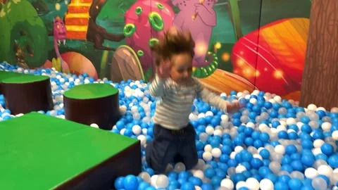 Slow motion footage of a little boy jumping into a pool with colorful balls Stock Footage 276468643