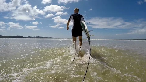 Slow motion footage of a surfer going towards the sea with a surfboard.  Vidéo 124599207