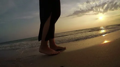 Slow-motion footage of a woman walking by the sandy beach at sunset Stock Footage