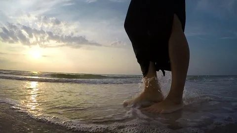 Slow-motion footage of a woman's feet stepping on the sand beach at sunset Stock Footage