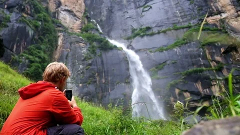 Slow-motion footage of a young guy shooting video of Jogini waterfall in India Vidéo 71119525