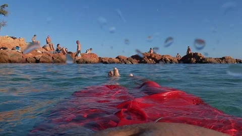 Slow motion FPV of man in red swimwear floating on calm sea Видео 280734594