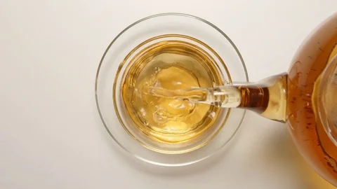 SLOW MOTION: Fresh tea flowing to a tea cup from a teapot - top view Видео 70572897