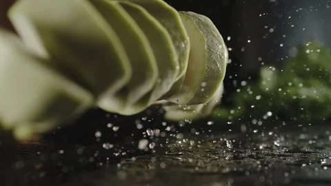 SLOW MOTION:  Fresh Zucchini Squash Slices Slpashing Down On A Wet Black Surface Stock Footage 115958445