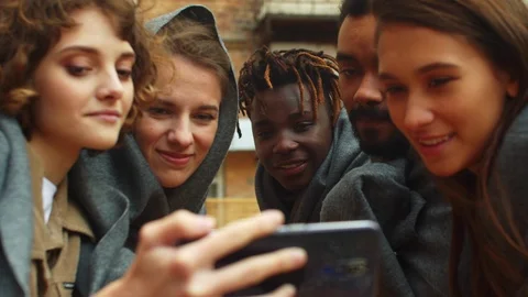 Slow motion, friends in blankets sit outside the cafe and look at photo on phone Stock Footage 121938403
