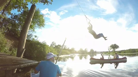 SLOW MOTION: Friends film playful man doing a backflip off rope swing into river Stock Footage