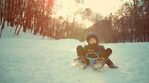 Slow motion of funny kid boy sliding on snow saucer sled outdoors in winter Stock Footage 148733287