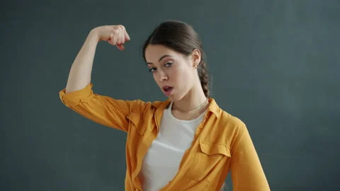 Slow motion of funny young lady showing muscles and moving arms smiling on gray Stock Footage 149660981