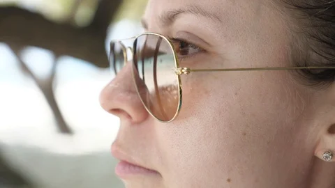 Slow Motion. Girl Adjusts the Frame of Glasses Looking at Sea with Palm Trees. Video stock 129549387