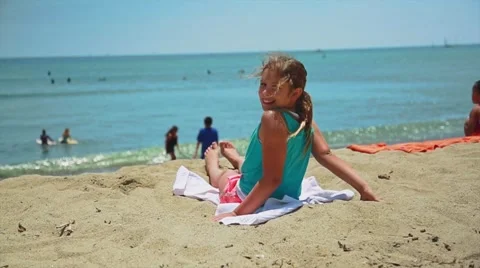 Slow motion of girl smiling at camera while sitting on the sand at beach Stock Footage 63749584
