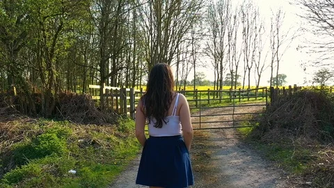 Slow motion of girl walking down path up to gate, looking over fields Stock Footage 108404100
