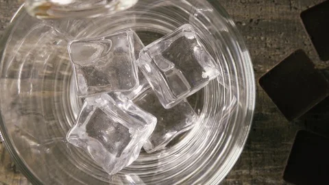 Slow motion in the glass with artificial ice pouring whisky top view Stock Footage 93992072