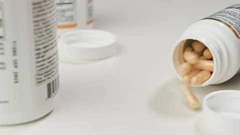 SLOW MOTION: a glass jar falls and yellow tablets fall out of it onto a white Stock Footage 153019953