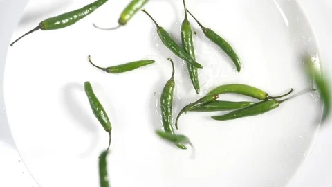 Slow motion green birdseye chillis falling onto a white plate surface Stock Footage 88340286