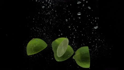Slow motion green lime halves falling into transparent water on black background Stock Footage 163786340