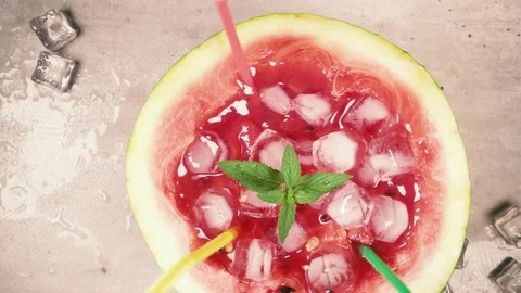Slow motion half watermelon with straws and ice rotating on the table top view Stock-Footage 93589604