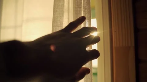 Slow motion hand moves towards a window curtain to reveal the sunlight outside Stock Footage