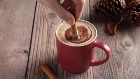 Slow motion of a hand stirring hot chocolate with a cinnamon stick in a cozy Stock Footage 345670111