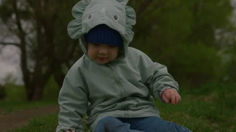 Slow motion handheld shot of a little boy sitting on the grass in a spring park Stock Footage 333143973