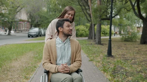 Slow motion of handicapped guy talking to young woman pushing wheelchair in city Stock Footage 156328450