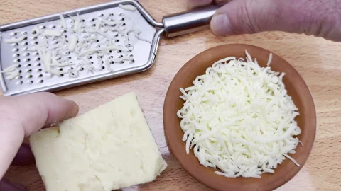 Slow motion of hands on a grater and piece of cheese next to some grated cheese. Stock Footage 300563752