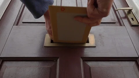 Slow motion: Hands posting a package / letter through a house letterbox. Stock-Footage 97500737