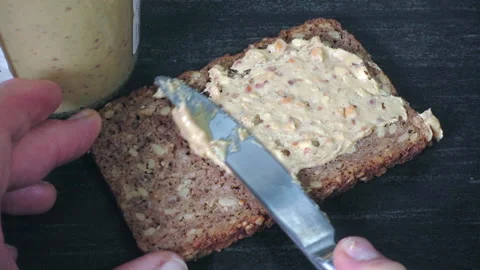Slow motion - Hands spreading crunchy peanut butter on a slice of rye bread. Video stock 195439726