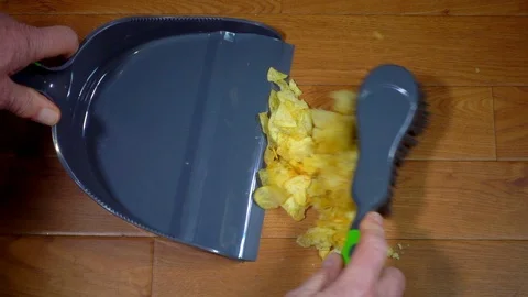 Slow motion: Hands using a dustpan and brush to sweep up potato crisps. Video stock 87283449