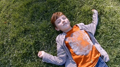 Slow motion happy red-haired boy lies the green grass in a park in a clearing, Stock Footage 118895202