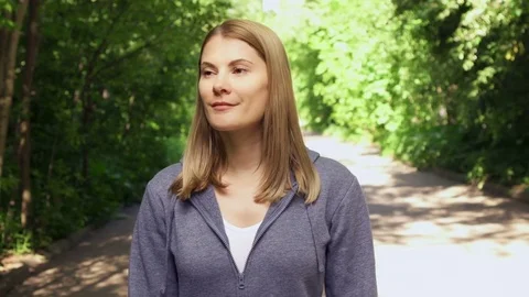 Slow Motion Happy smiling young woman in hoodies walking around in sunny park on Stock Footage 76847955