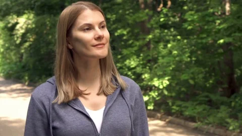 Slow Motion Happy smiling young woman in hoodies walking around in sunny park on Stock Footage 76980231