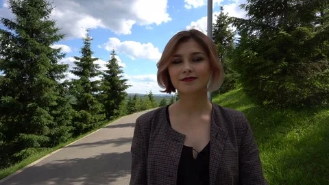Slow Motion Happy smiling young woman in jacket walking around in sunny park on Stock Footage 77657202