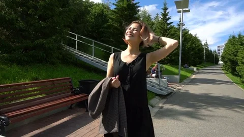Slow Motion Happy smiling young woman in black dress walking around in sunny Stock Footage 77658244
