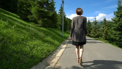Slow Motion Happy smiling young woman in jacket walking around in sunny park on Stock Footage 77720507
