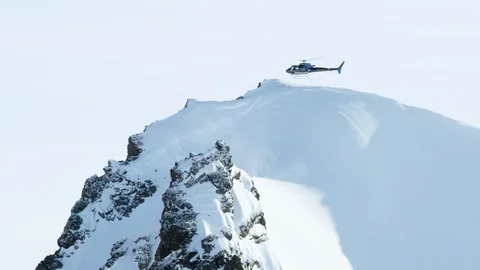 Slow motion of helicopter flying over summit in snow in Alaskan mountains Stock Footage 129111025