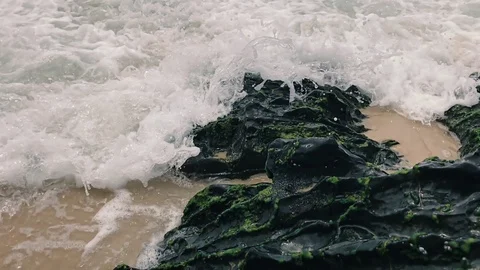 Slow motion high speed waves crashing into moss covered rocks on beach. 스톡 동영상 71317596