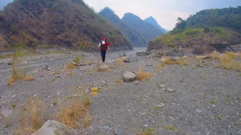 Slow motion of a hiker walking on wide opening riverbed with pile of colorful co Stock Footage 266502575