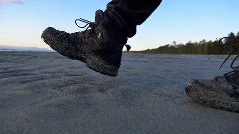 Slow motion hiking boots from side walking along beach in shallow water. Stock Footage 129659123